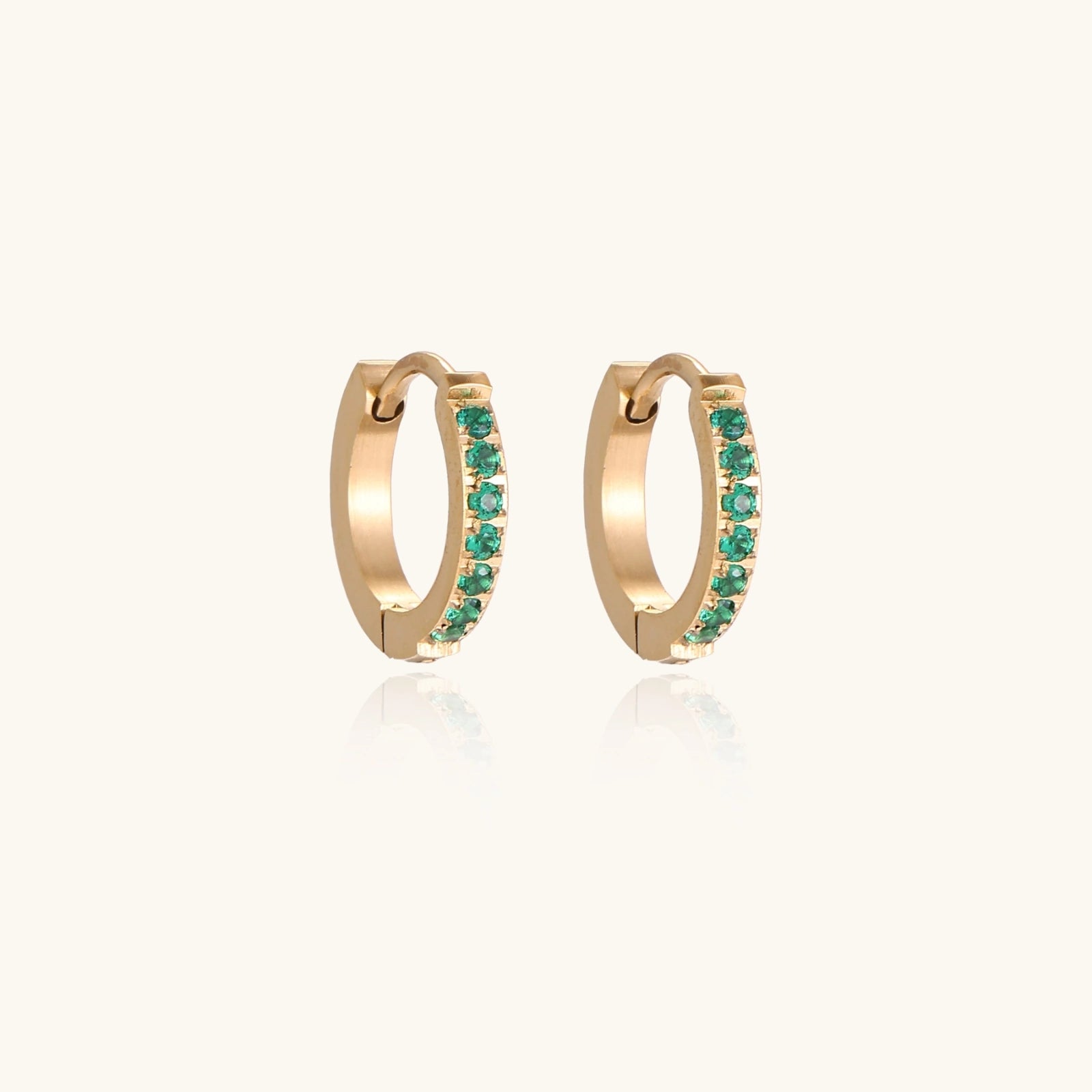 Pair of small gold huggie hoop earrings with bright green cubic zirconia stones on cream background