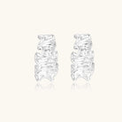 Textured white gold-plated hoop earrings with flowing wave pattern against cream background, showing dimensional rippled surface.