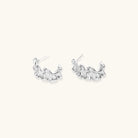Textured white gold-plated hoop earrings with flowing wave pattern against cream background, showing dimensional rippled surface.