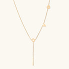 Gold Y-shaped necklace with L-O-V-E letter charms and vertical bar pendant on delicate chain against cream background