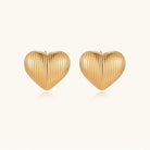 Gold heart-shaped stud earrings with parallel ridged texture on cream background