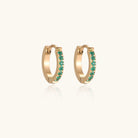 Pair of small gold huggie hoop earrings with bright green cubic zirconia stones on cream background
