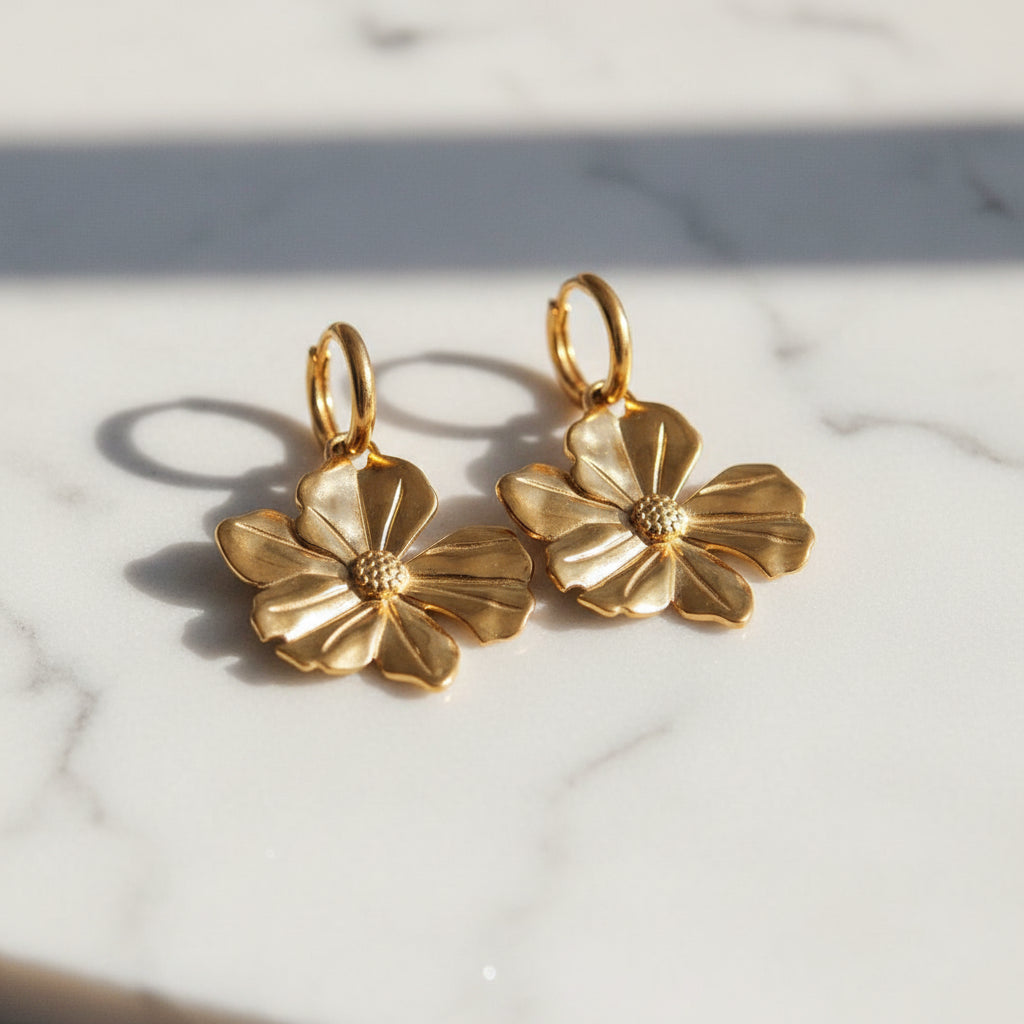 Gold floral earrings on a marble surface