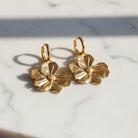 Gold floral earrings on a marble surface