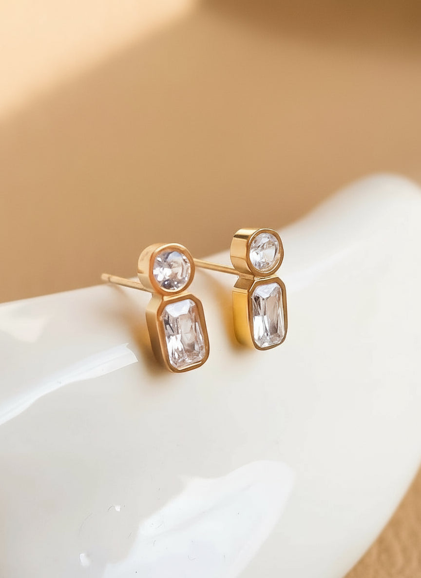 Gold earrings with clear gemstones on a white surface